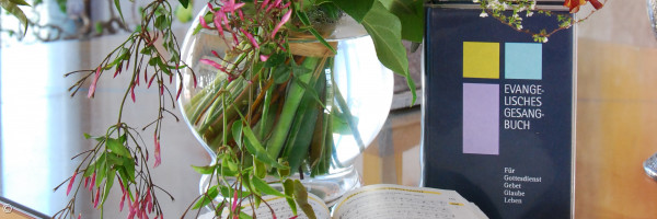 Ein evangelisches Gesangbuch steht auf dem Alter neben einem Blumenstrauß, ein weiteres liegt aufgeschlagen davor.