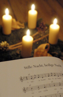 Die Noten von "Stille Nach, heilige Nacht", im Hintergrund ein Adventskranz mit vier Kerzen